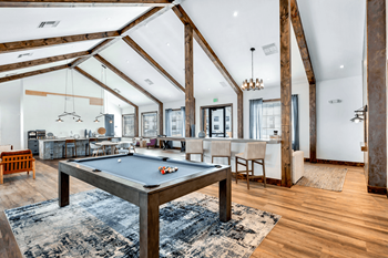 A pool table in the center of a living room with a kitchen and a bar